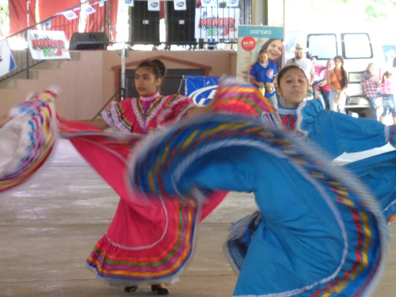 Two young dancers in pink and blue folklórico dresses spinning their skirts